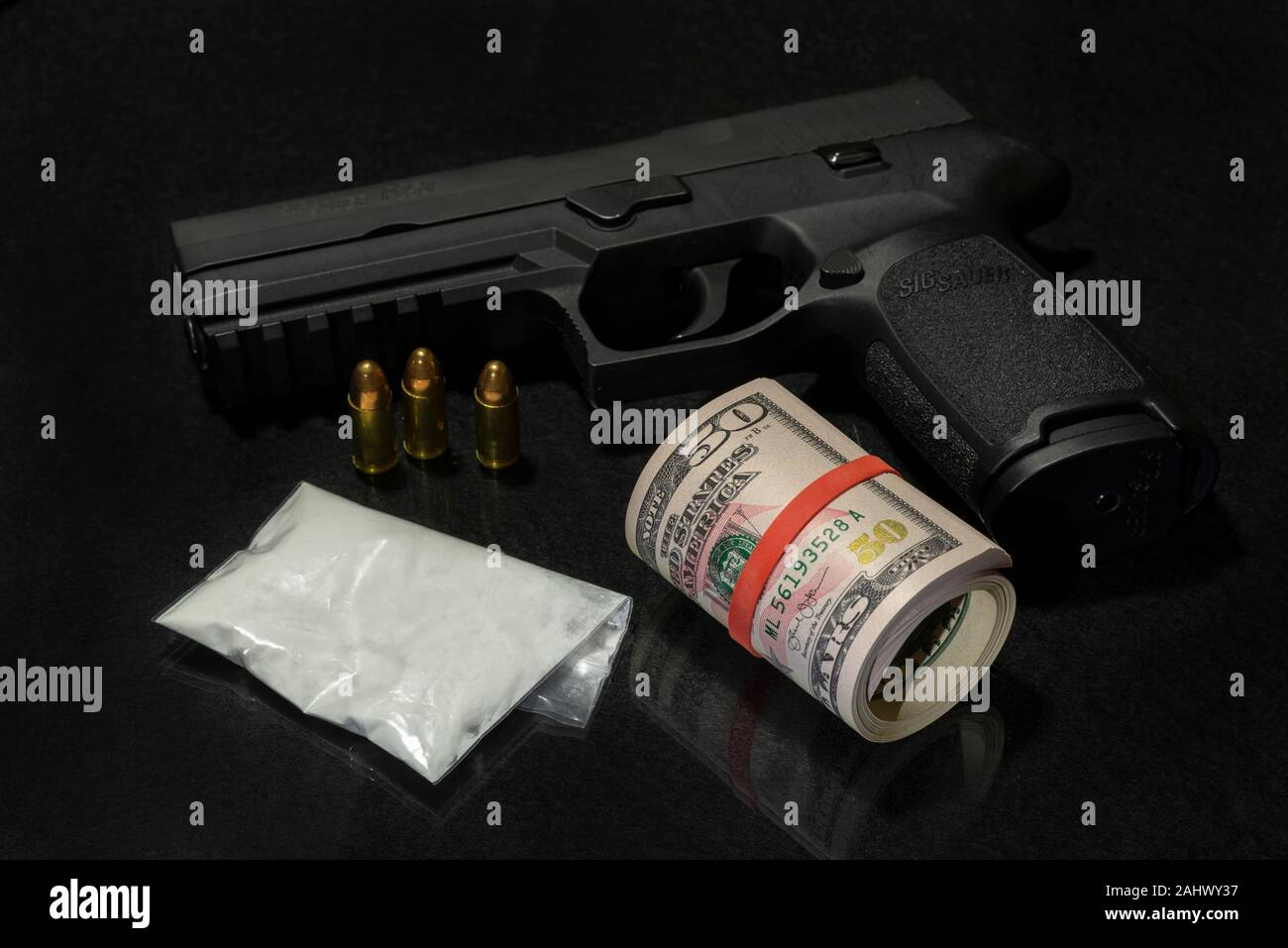 Bag of powdered drugs with a Sig Sauer handgun and a roll of $50 dollar bills on a black background. Stock Photo