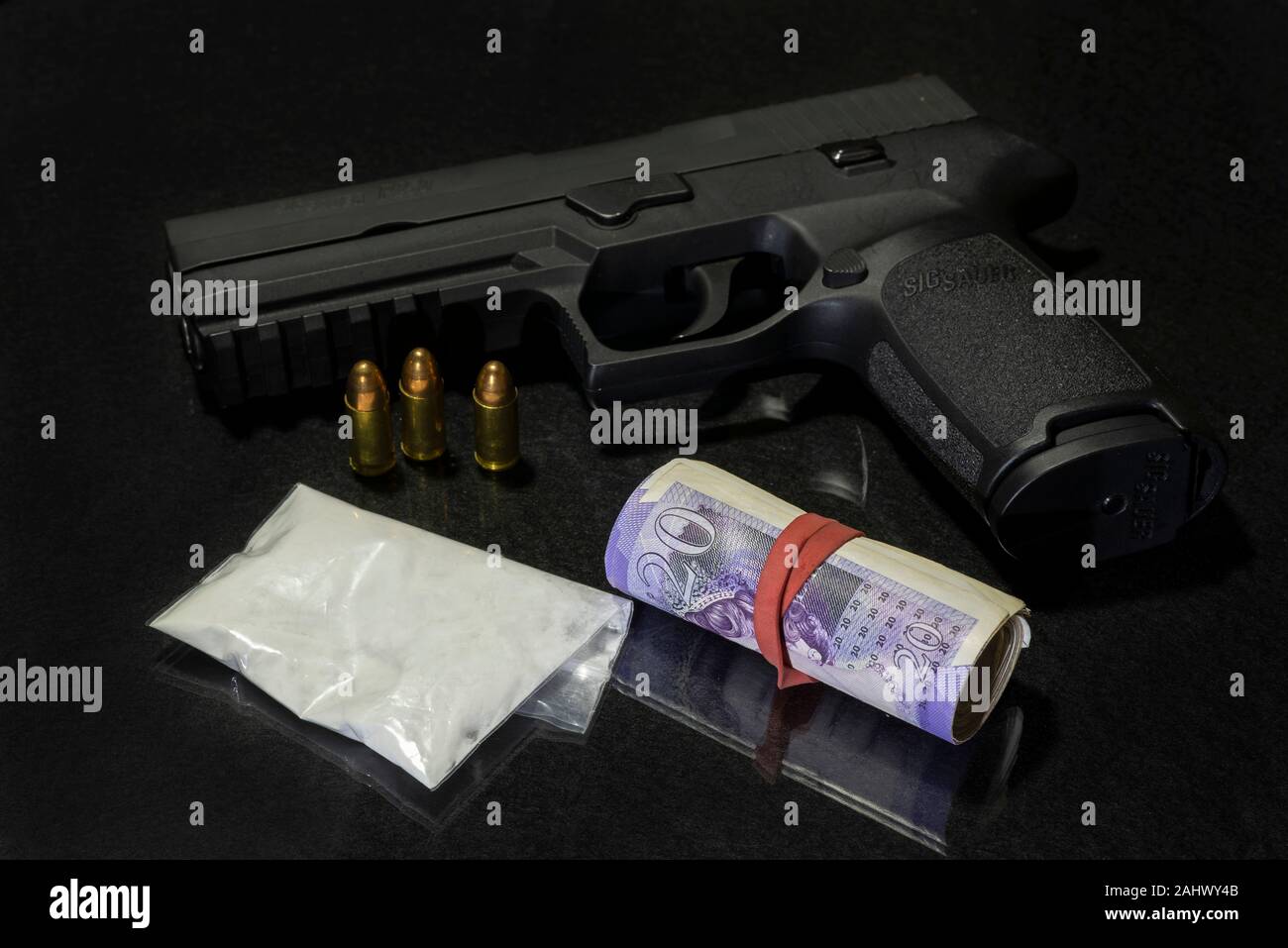 Bag of powdered drugs with a Sig Sauer handgun and a roll of  £20 pound notes (GBP)  on a black background. Stock Photo