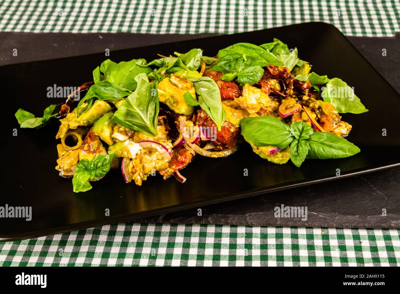 Dressed Salad on black plate with avocado, sun dried tomato, red onion, feta and basil, landscape on plate on slate Stock Photo