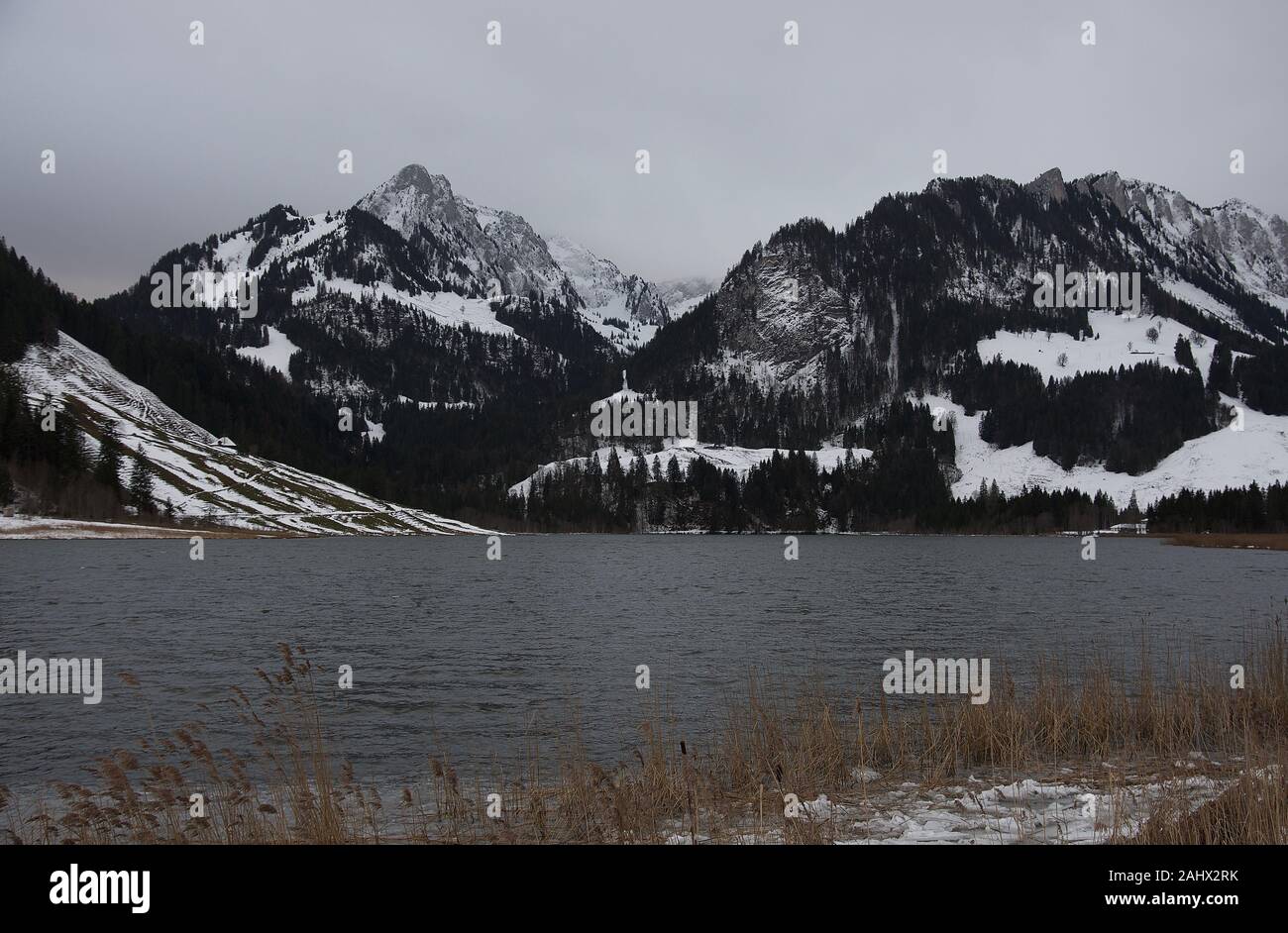 Foggy mountain range behind dark lake in winter Stock Photo