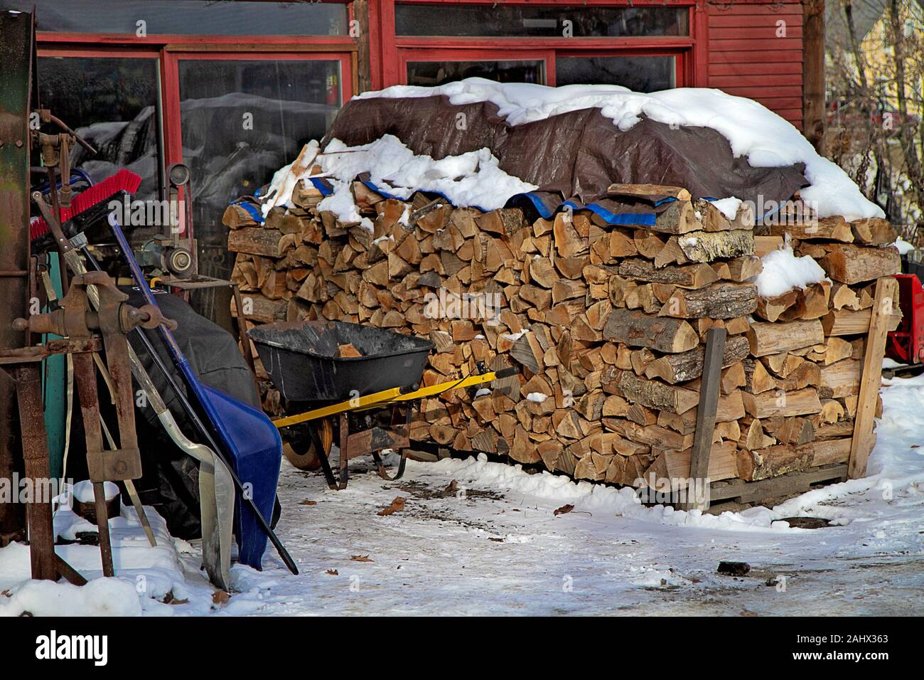 Fire Wood stacked high outside and behind a building in the midst of winter with snow on the ground and covering wood. Stock Photo