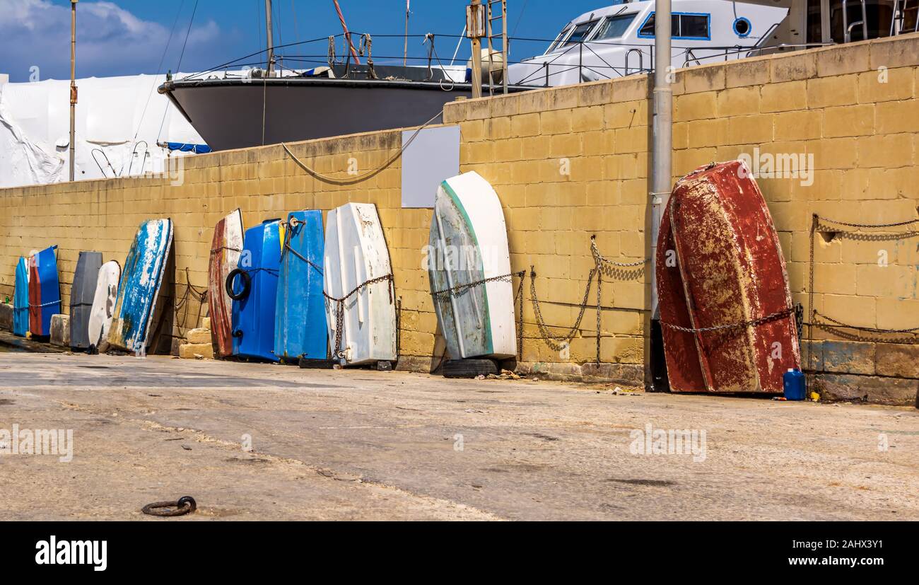 Row of multicolored wooden fishing boats leaned and tied up against the wall in Gzira, Malta. Stock Photo