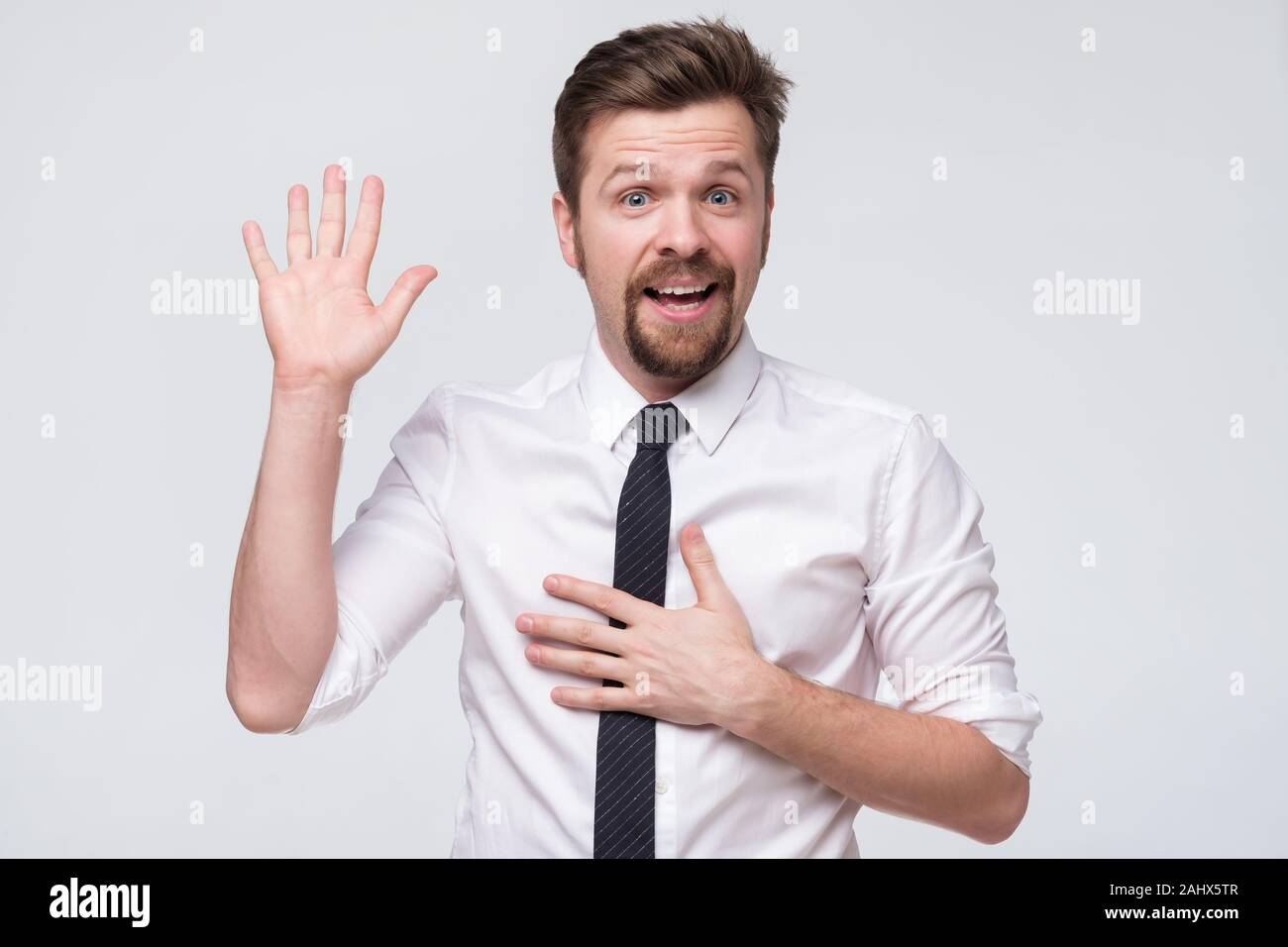 Young caucasian man in white shirt swearing with hands on chest and open palm, making a loyalty promise Stock Photo