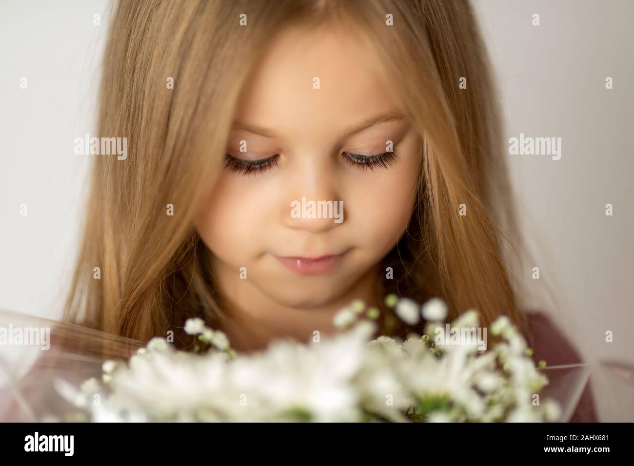 close-up portrait of a blonde little girl with downcast eyes holding a bouquet of white wildflowers Stock Photo