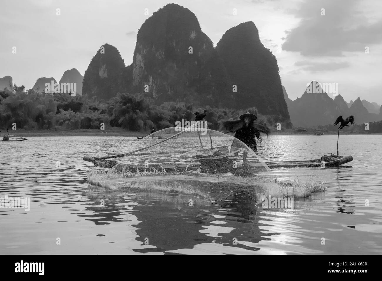 Cormorant fisherman throwing a cast net at sunset on the Li River by the karst mountains.Guilin, China Stock Photo