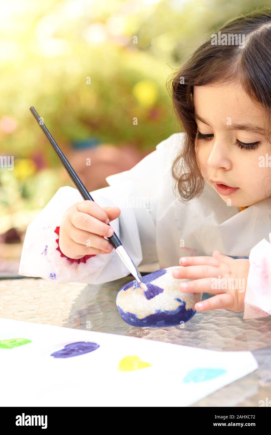 Portrait of little child painting on stone with blue color. Kid drawing on a stone, summer outdoor. Stock Photo