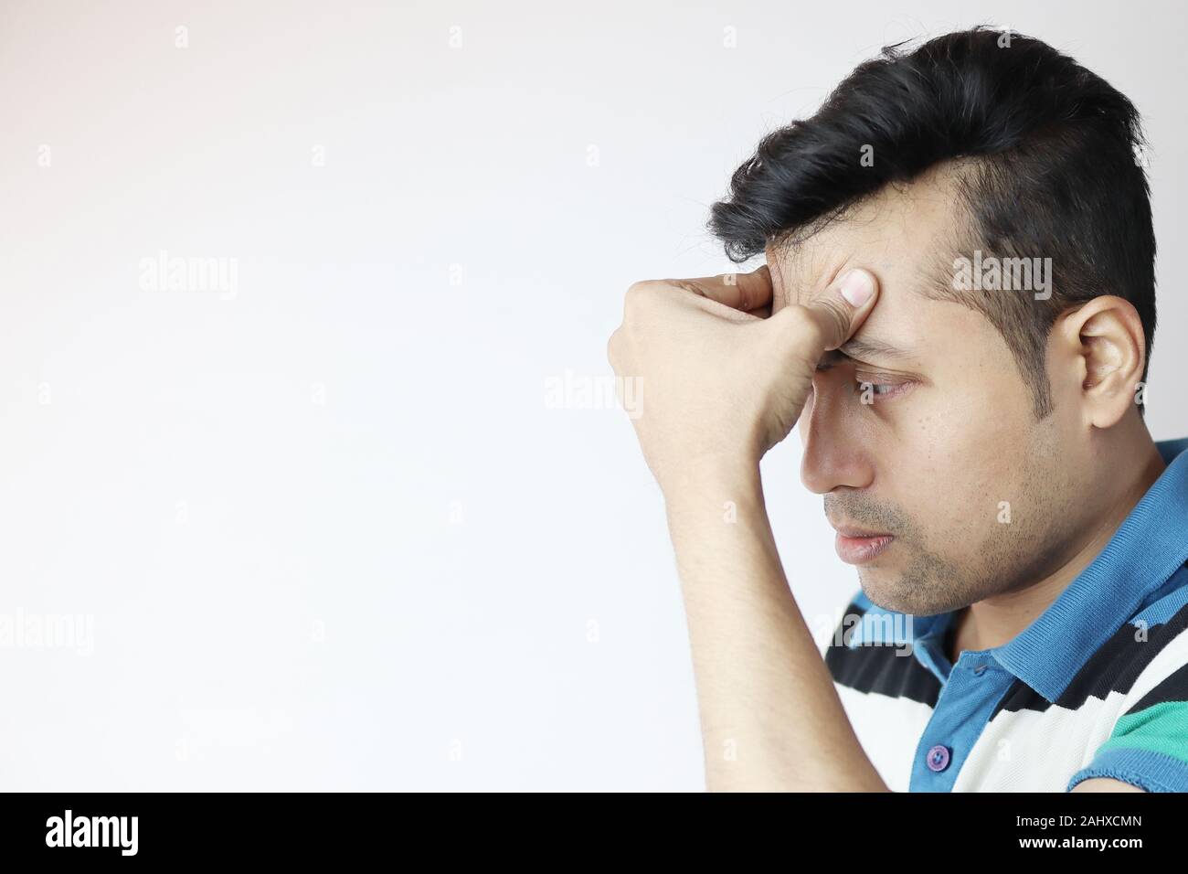 a young indian male with hands on forehead with a very worried expression isolated on white with copy space for text Stock Photo
