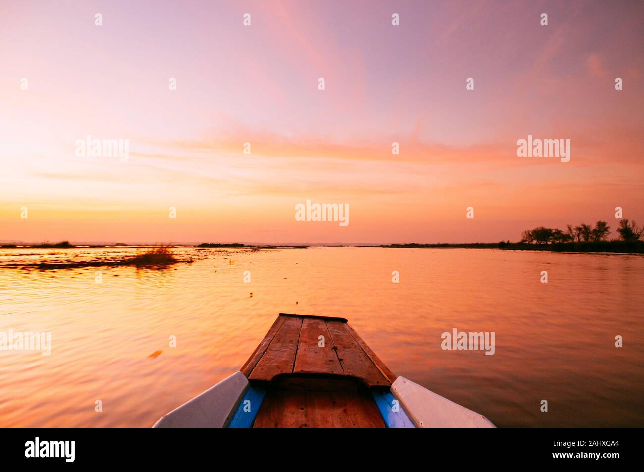 Thai long tail boat front bow in peaceful Nong Harn lake, Udonthani - Thailand. Wooden boat under vibrant beautiful sunrise sky over red lotus lake. Stock Photo