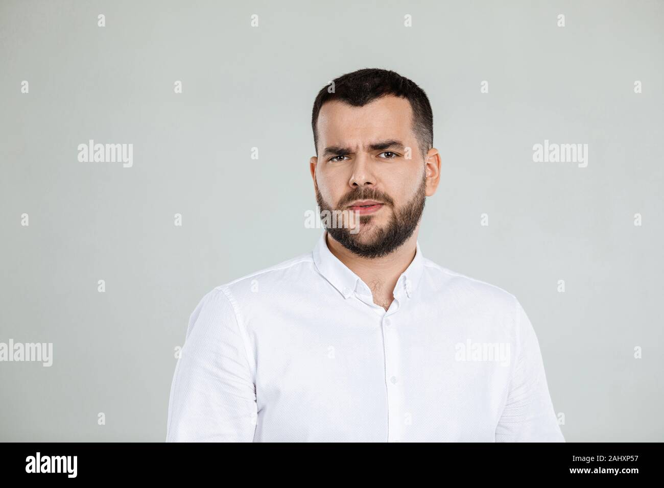 Portrait of young frowned handsome bearded man on gray background. facial expression Stock Photo