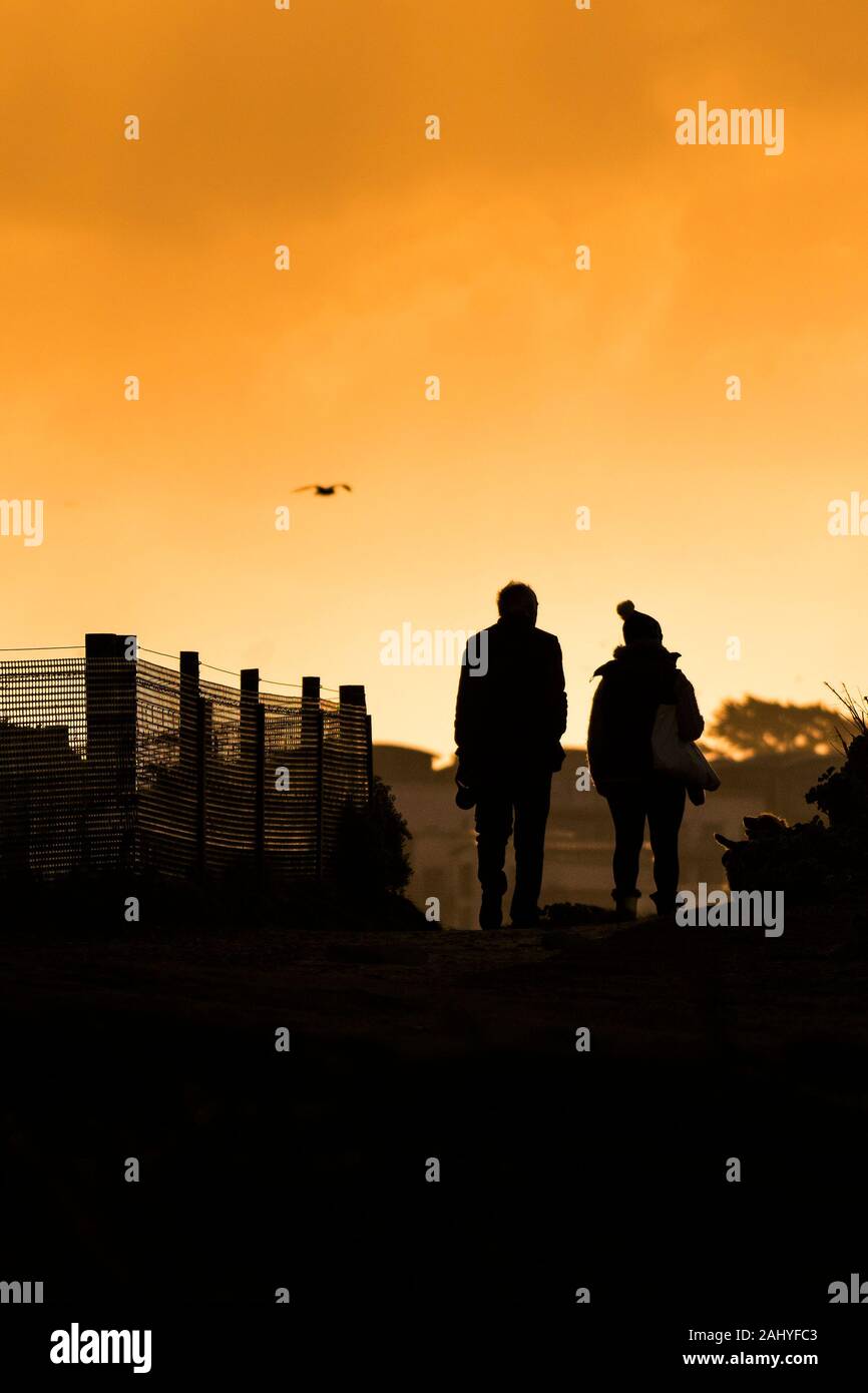 The silhouette of two people walking in evening light. Stock Photo