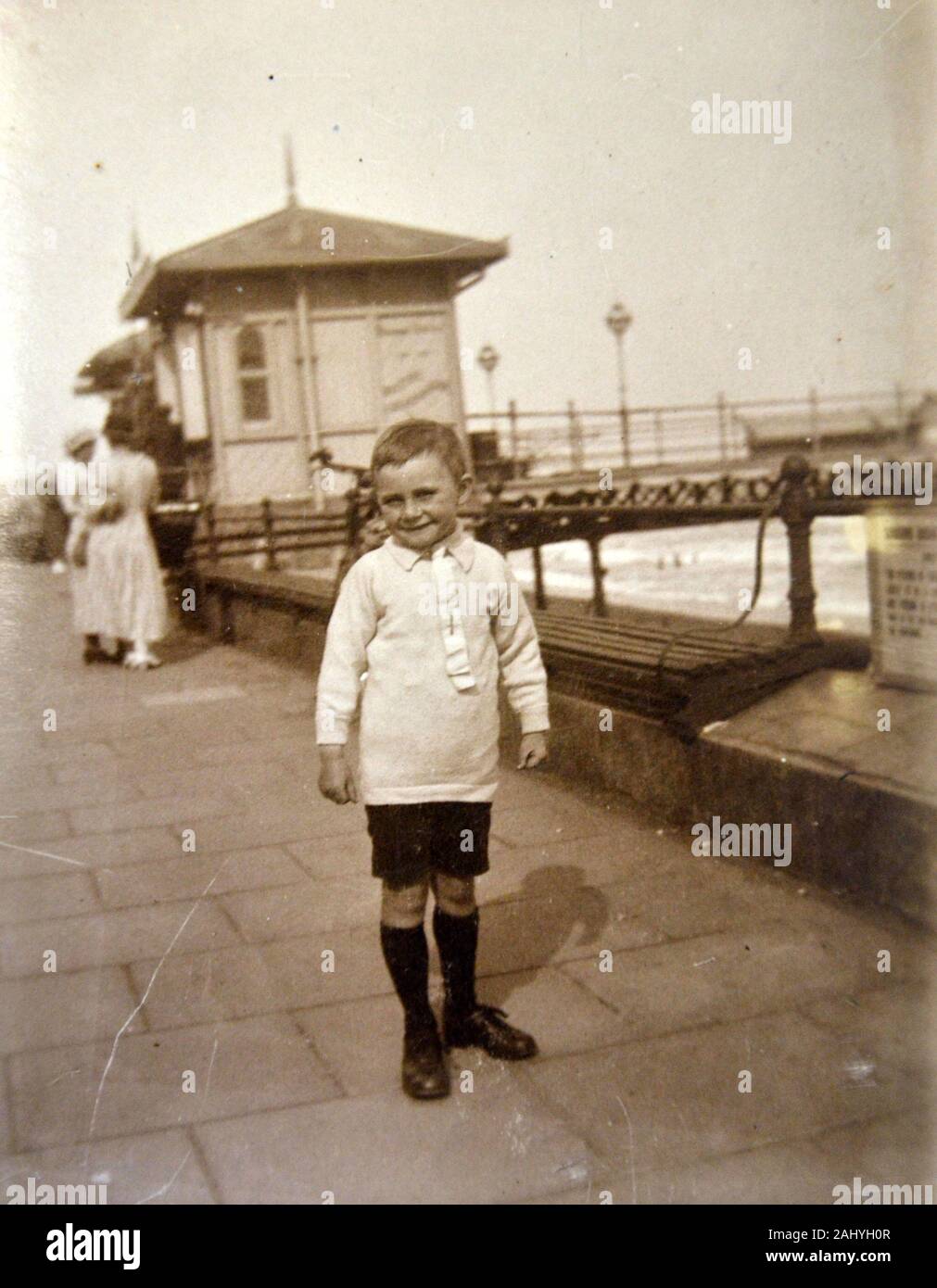 Old vintage black and white photograph of a young boy standing in front of a seaside pier Stock Photo