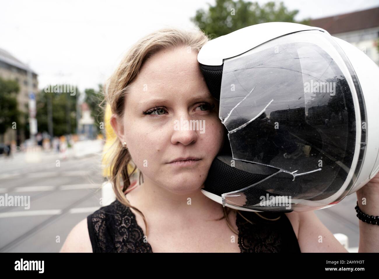 Woman holding motorcycle helmet with a shattered visor, Munich, Germany