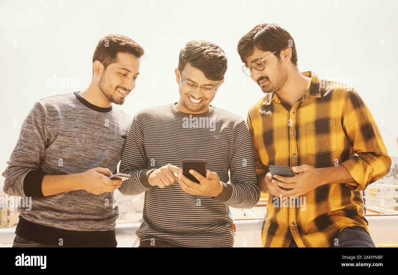 Group of young people watching mobile phone on terrace and laughing - friends using mobile phone againt the sunlight - Millennials on technology Stock Photo