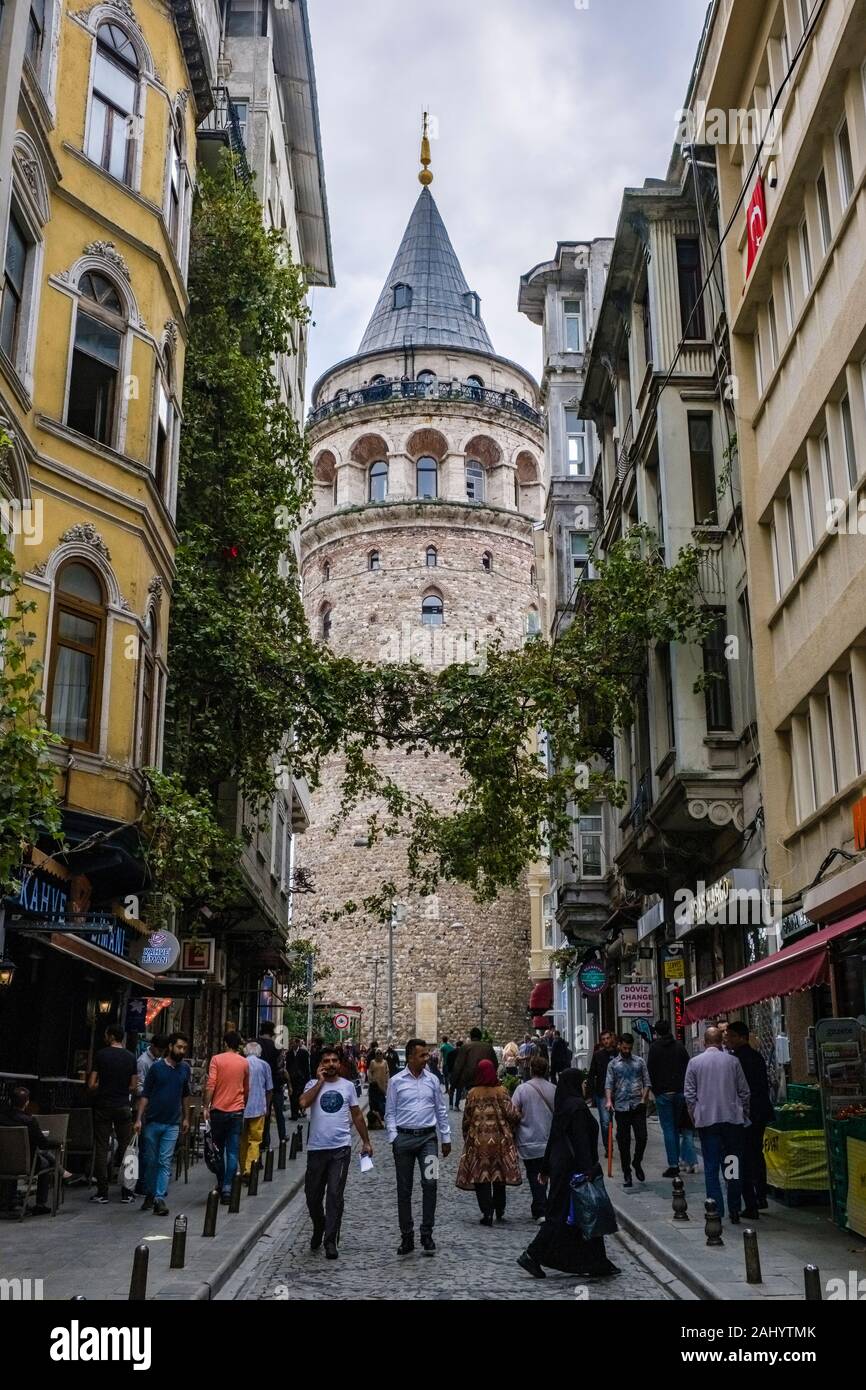 People waking in a small street, the Galata Tower, Galata Kulesi, a medieval stone tower in the distance Stock Photo