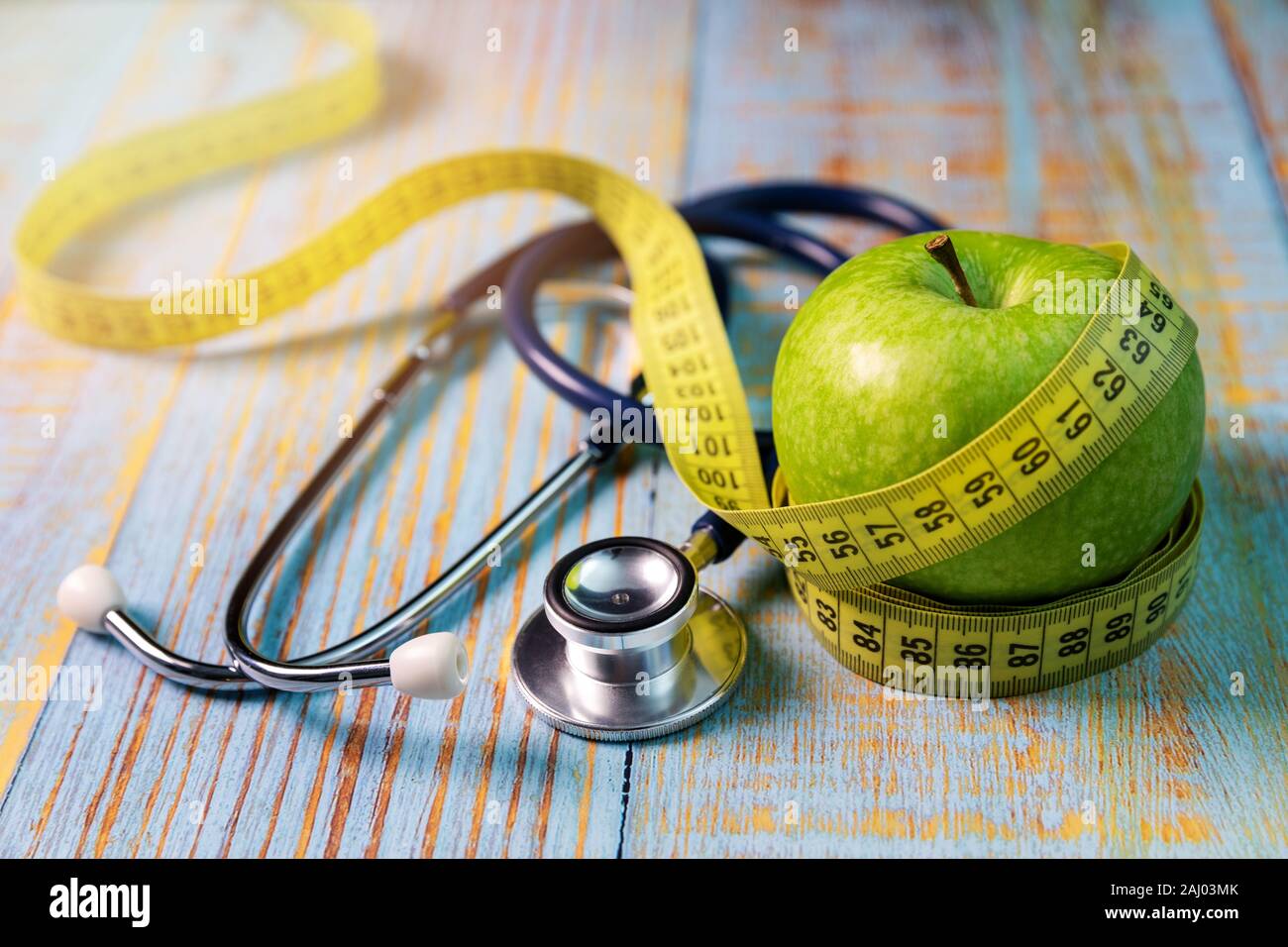 healthy lifestyle and nutrition concept - apple with measurement tape and stethoscope on the blue wooden table Stock Photo