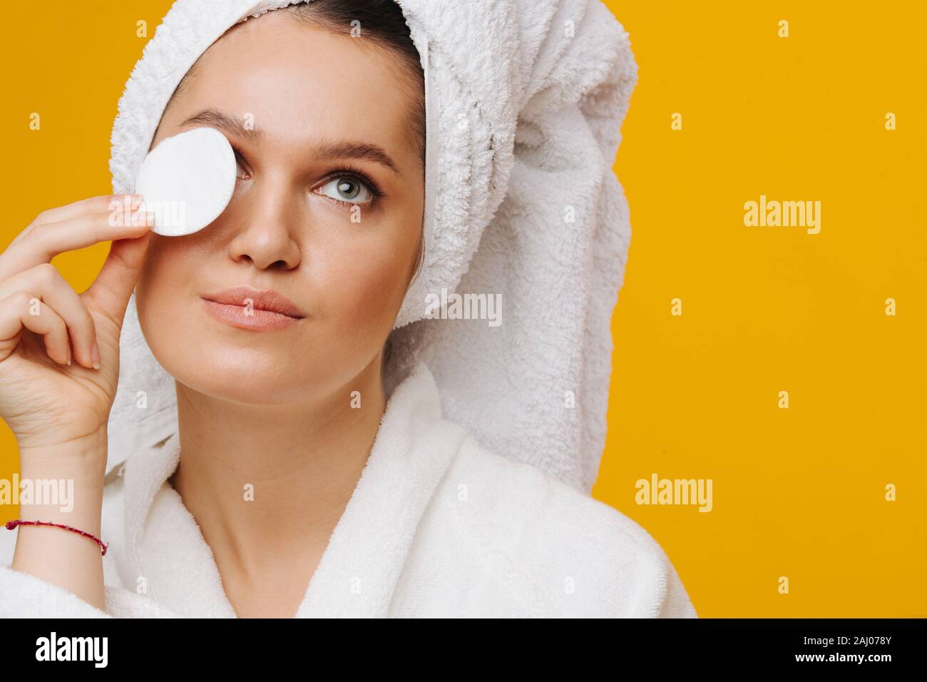 Woman with cotton disc moisturising her eyelids over yellow background. Stock Photo