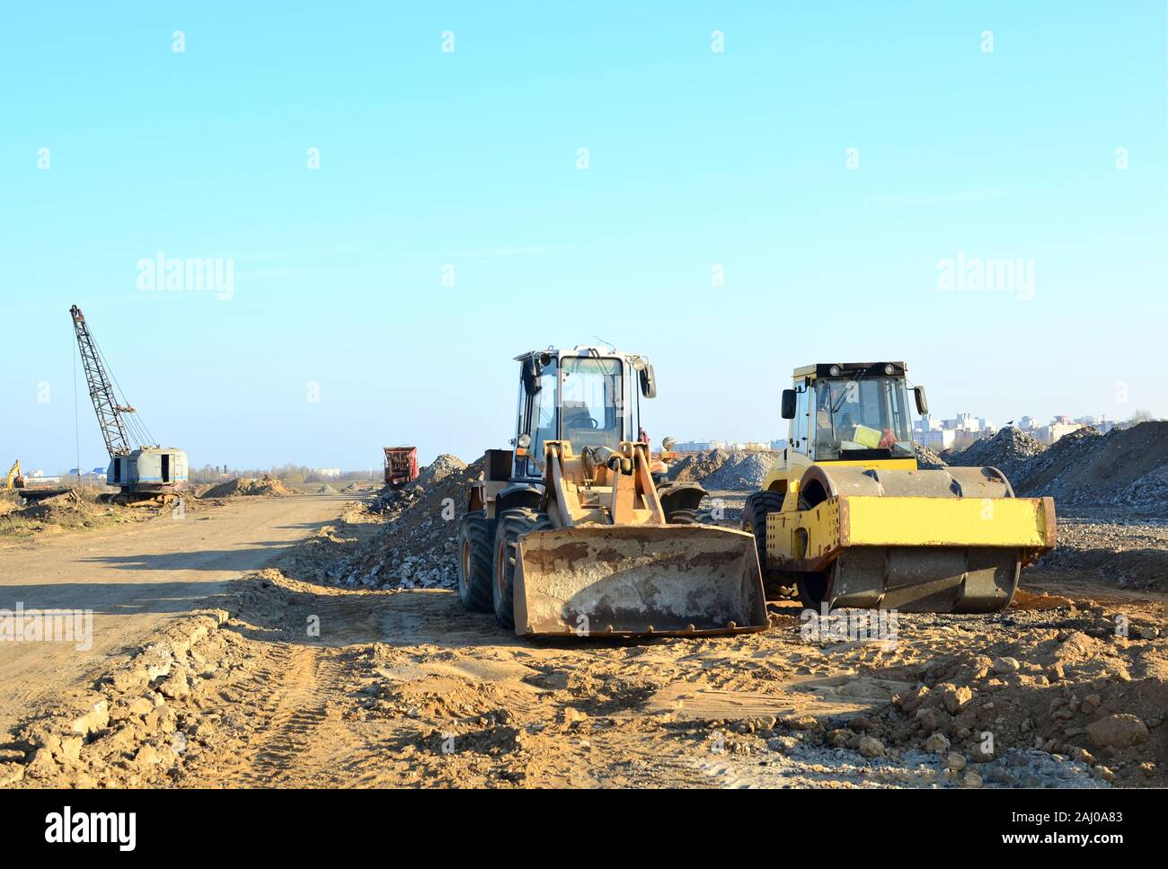 Soil Compactor and  wheel loader at construction site. Vibration single-cylinder road roller leveling the ground for the construct of the foundation f Stock Photo