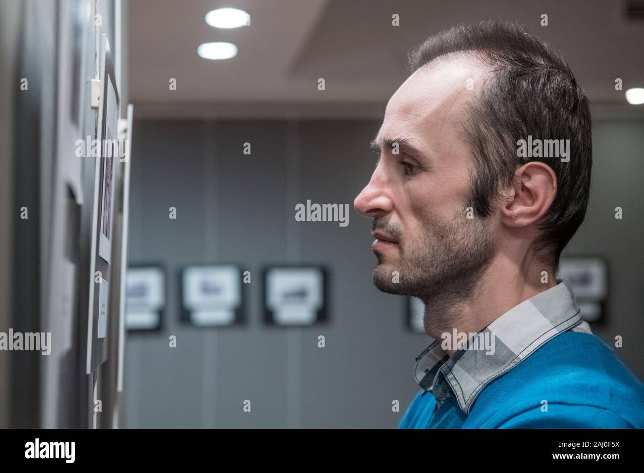 Side view of Caucasian man standing in an art gallery in front of black and white framed photos displayed on a gray wall. Stock Photo