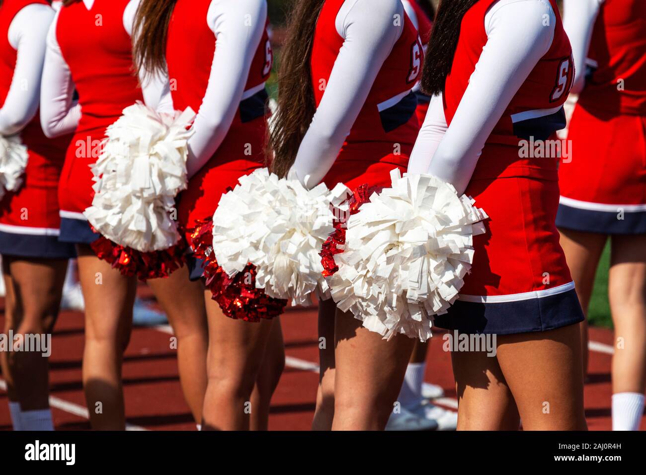 Rear view of high school cheerleaders standing with their pom poms behind them during a football game. Stock Photo