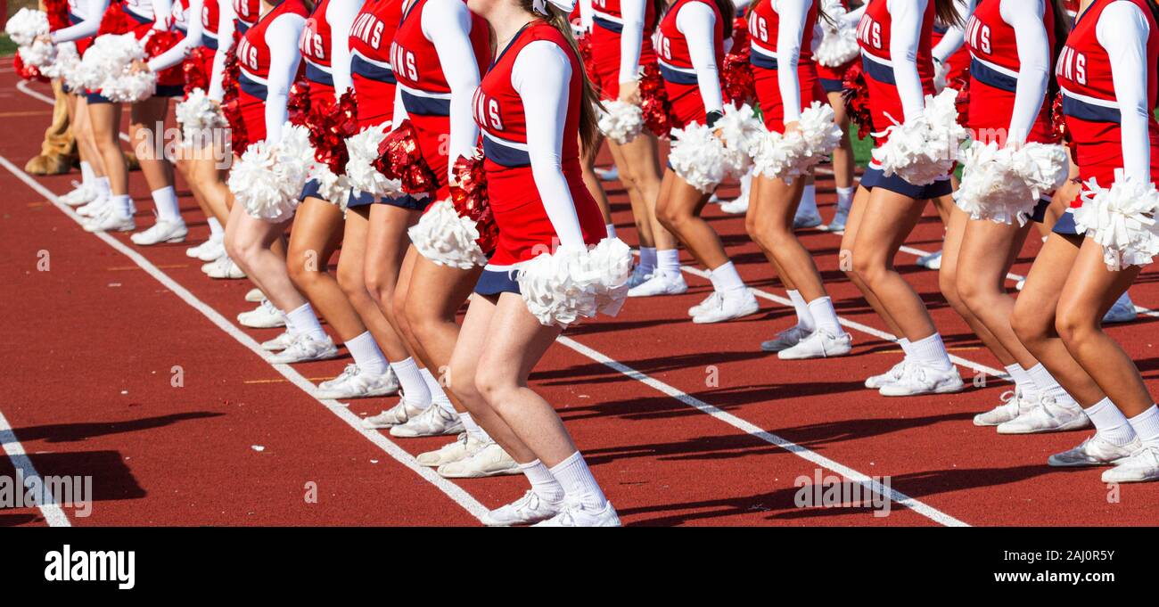 A high school cheerleading team is synchronized on a red track while performing for the fans furing a football game. Stock Photo