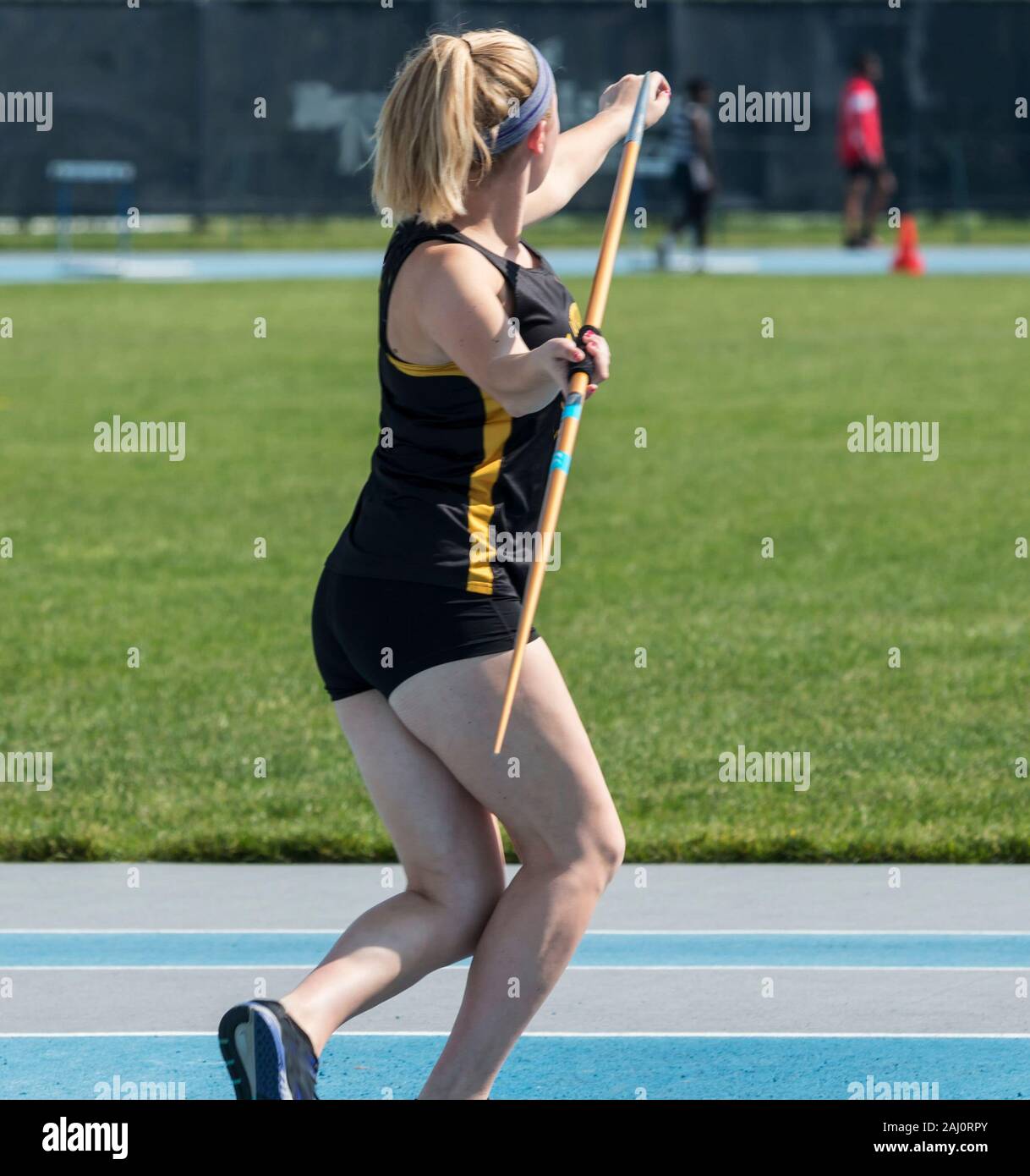 A view from behind a high school girl throwing a javelin out to a green grass field at a track and field competition. Stock Photo