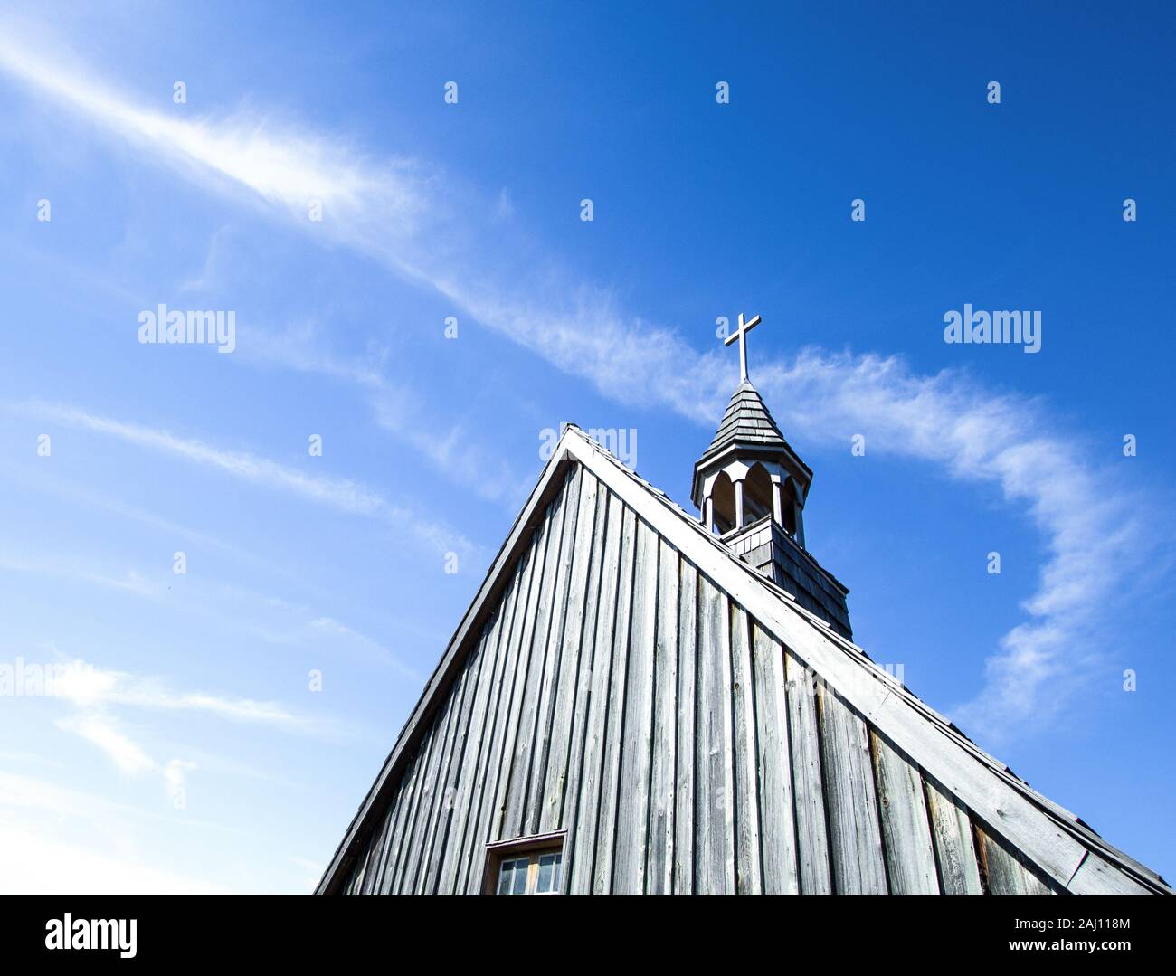 Church Steeple And Copy Space. Church steeple with wooden cross set against a blue sky with clouds and chem trails. Stock Photo