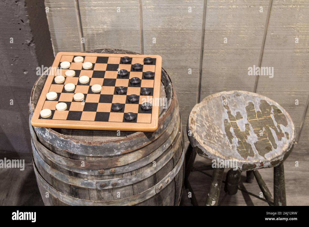 Old Fashioned Game Of Checkers. Checkerboard game with checkers on an old wooden keg barrel with old wood stool. Stock Photo