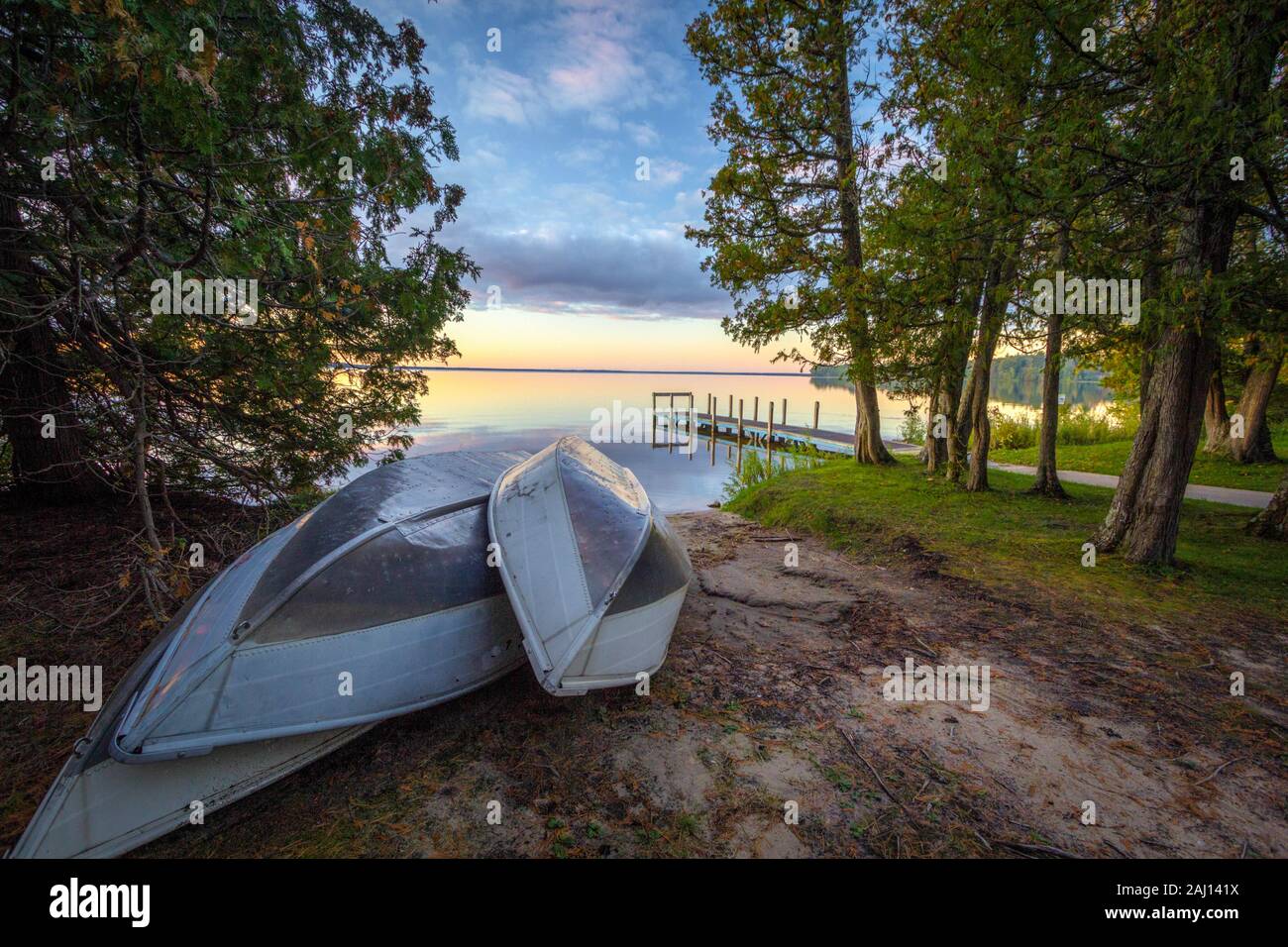 Rowboats On Sunset Lake. Group of aluminum rowboats on the beach of a sunset lake with a wooden dock in the background. Indian Lake State Park. Stock Photo