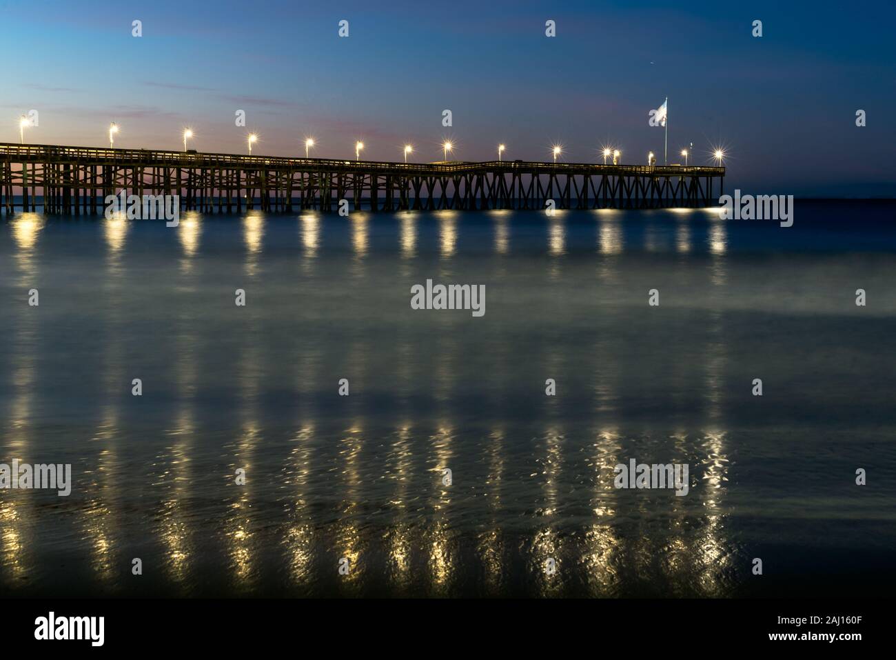 Lamp lights reflected in the ocean water below the Ventura Pier as dawn adds colors to the morning sky. Stock Photo