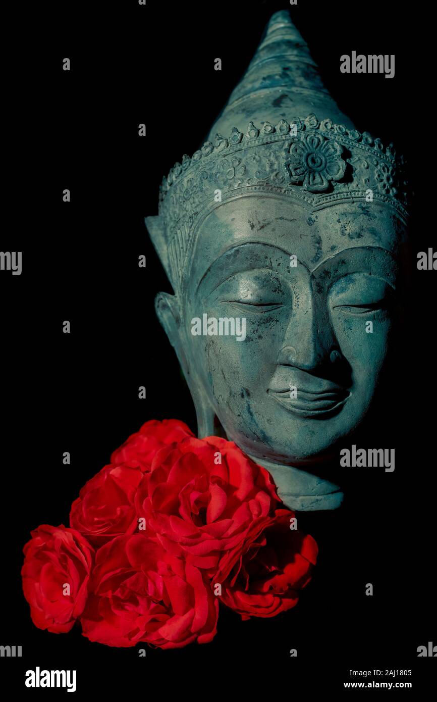 Spiritual love and enlightenment. Beautiful traditional blue buddha head statue with deep red rose flowers against black background. Aesthetic modern Stock Photo