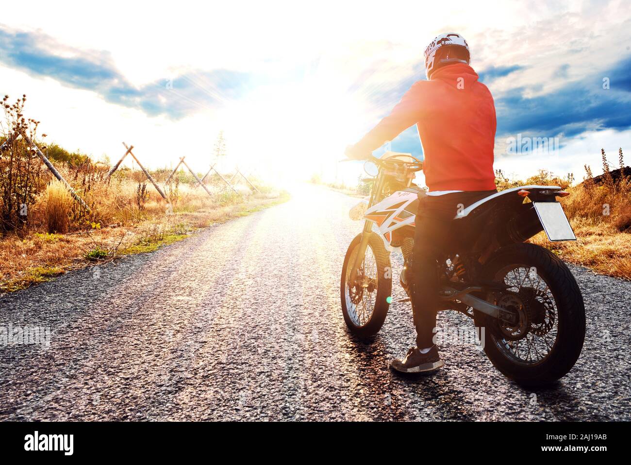 Young man driving with his motorbike on a street, looking in the sunset and enjoying the freedom and active lifestyle. Stock Photo
