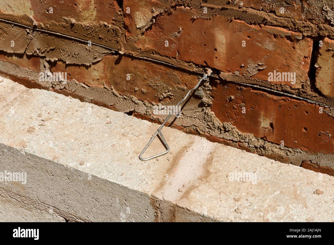 Close up detail of a cavity wall on a UK building site showing the damp proof course and a metal wall tie Stock Photo