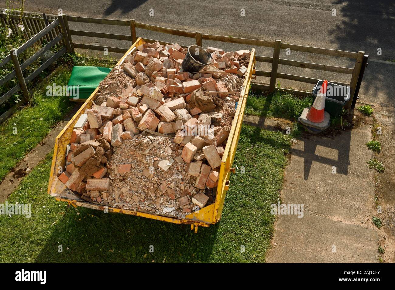 A skip full of building site rubble and bricks in the front garden of a