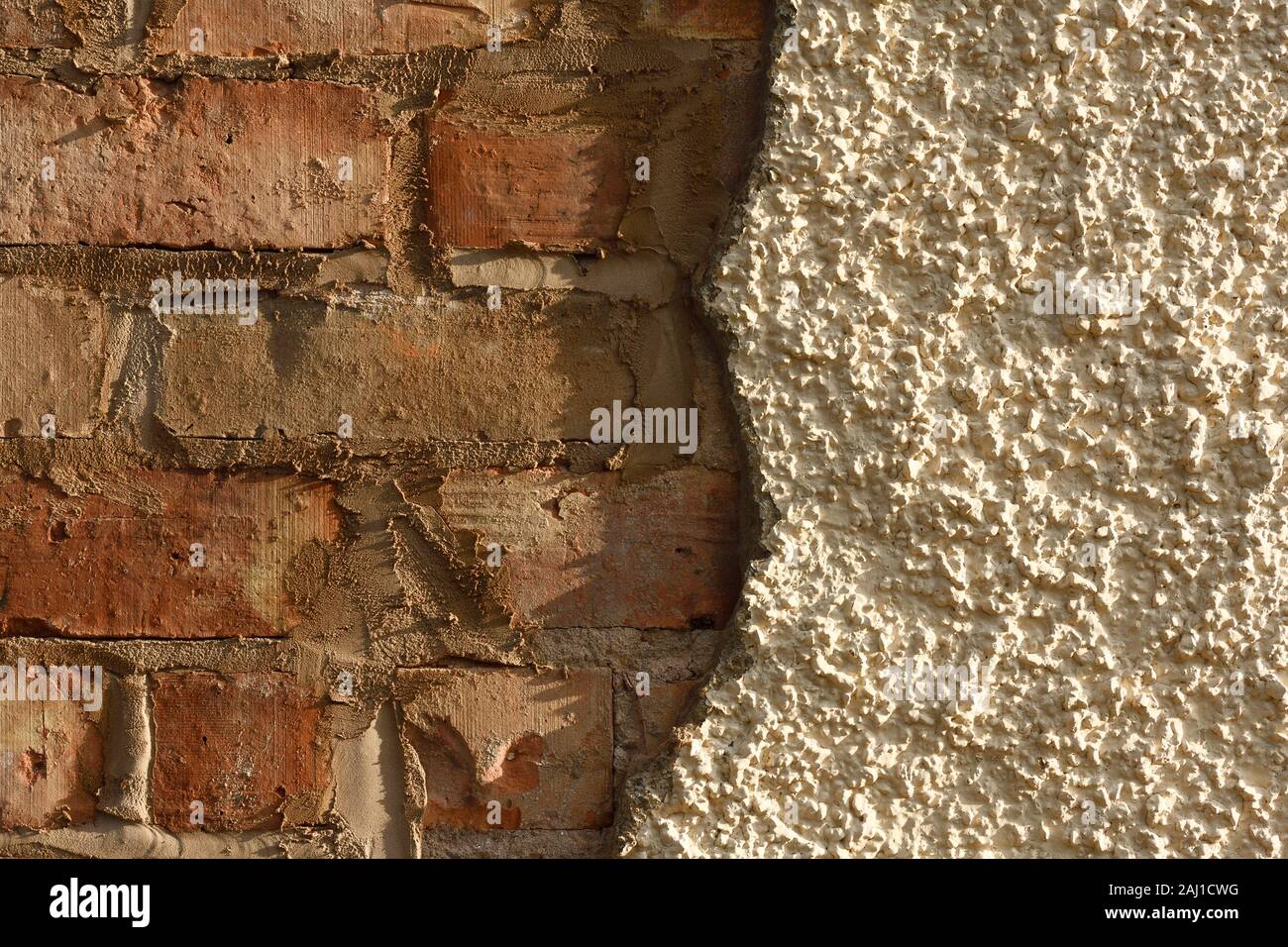 An exterior brick wall with half of the pebble dash render missing Stock Photo