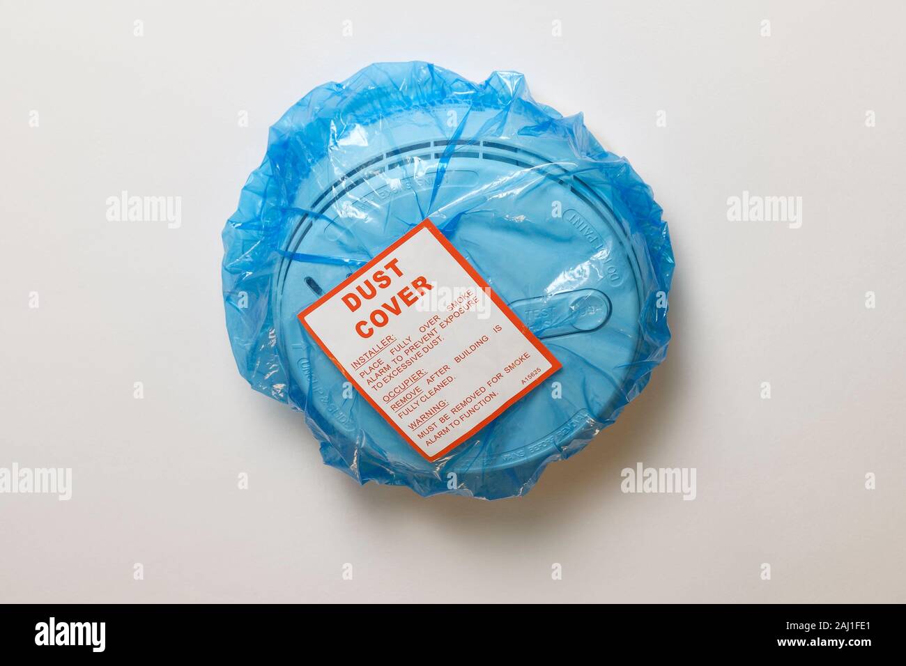 A blue polythene dust cover on a mains wired smoke alarm fitted in a UK domestic property Stock Photo