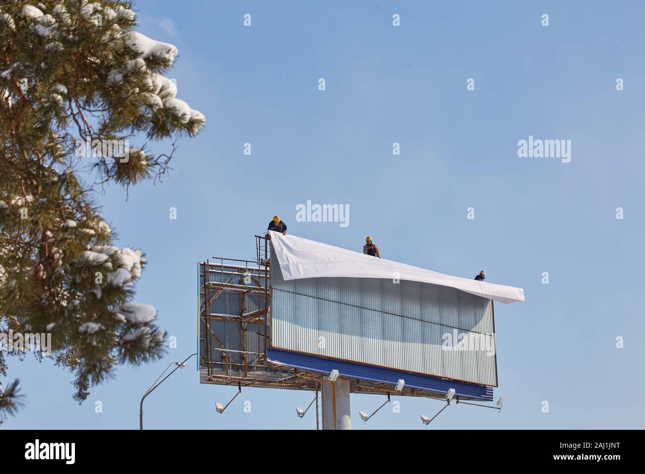 Worker prepares billboard to installing new advertisement. Industrial climber working on a ladder - placing an advertising banner. Stock Photo