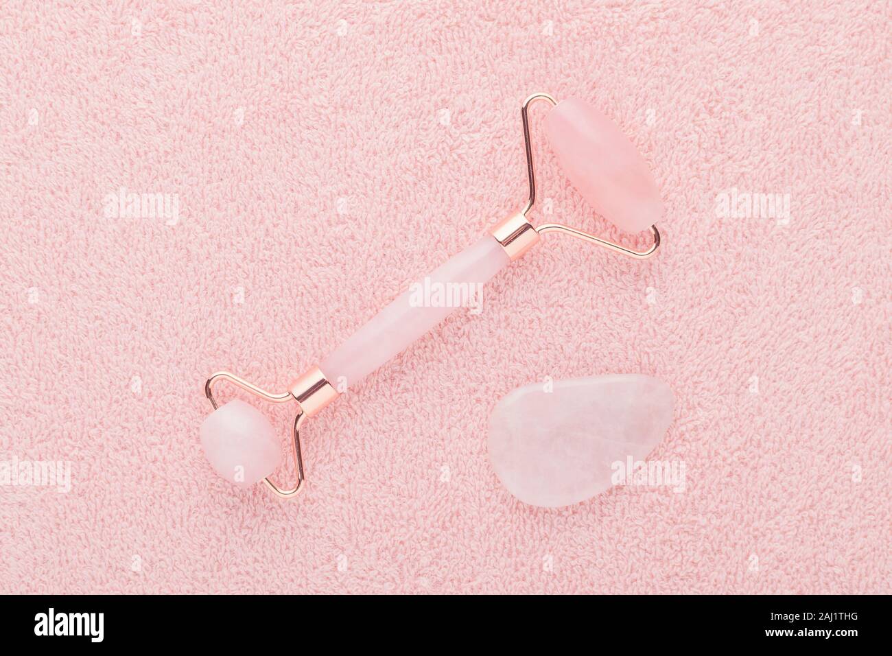 real rose quartz facial roller and gua sha stone on pastel pink background, flat lay Stock Photo