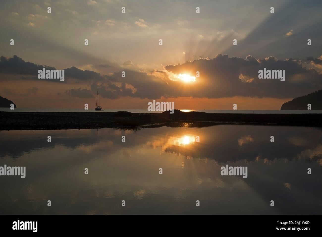 Wonderful sunrise and sunbeams at The Beach Of Adrasan, Antalya Province at Turkey. There was  a little pond at the beach and sky was reflecting. Stock Photo