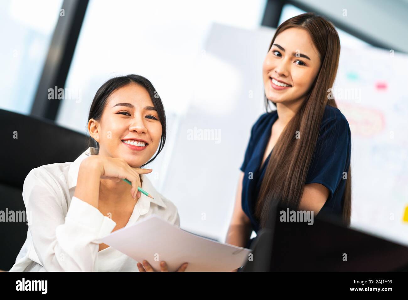 Portrait of two beautiful Asian office coworkers smiling together at work. Business colleagues, teamwork partner, job consultant, or working woman Stock Photo