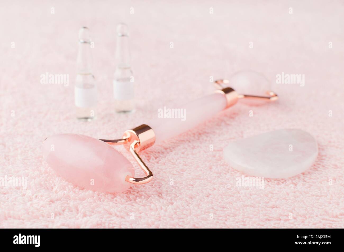 rose quartz facial roller, massage stone and face serum in ampoules, selective focus Stock Photo
