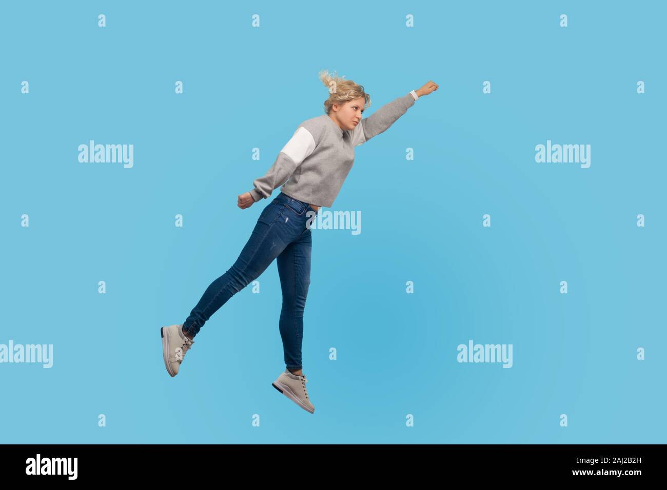 Superman. Full length portrait of determined woman in sweatshirt and jeans flying up in air, feeling superpower and freedom, trampoline to success. in Stock Photo