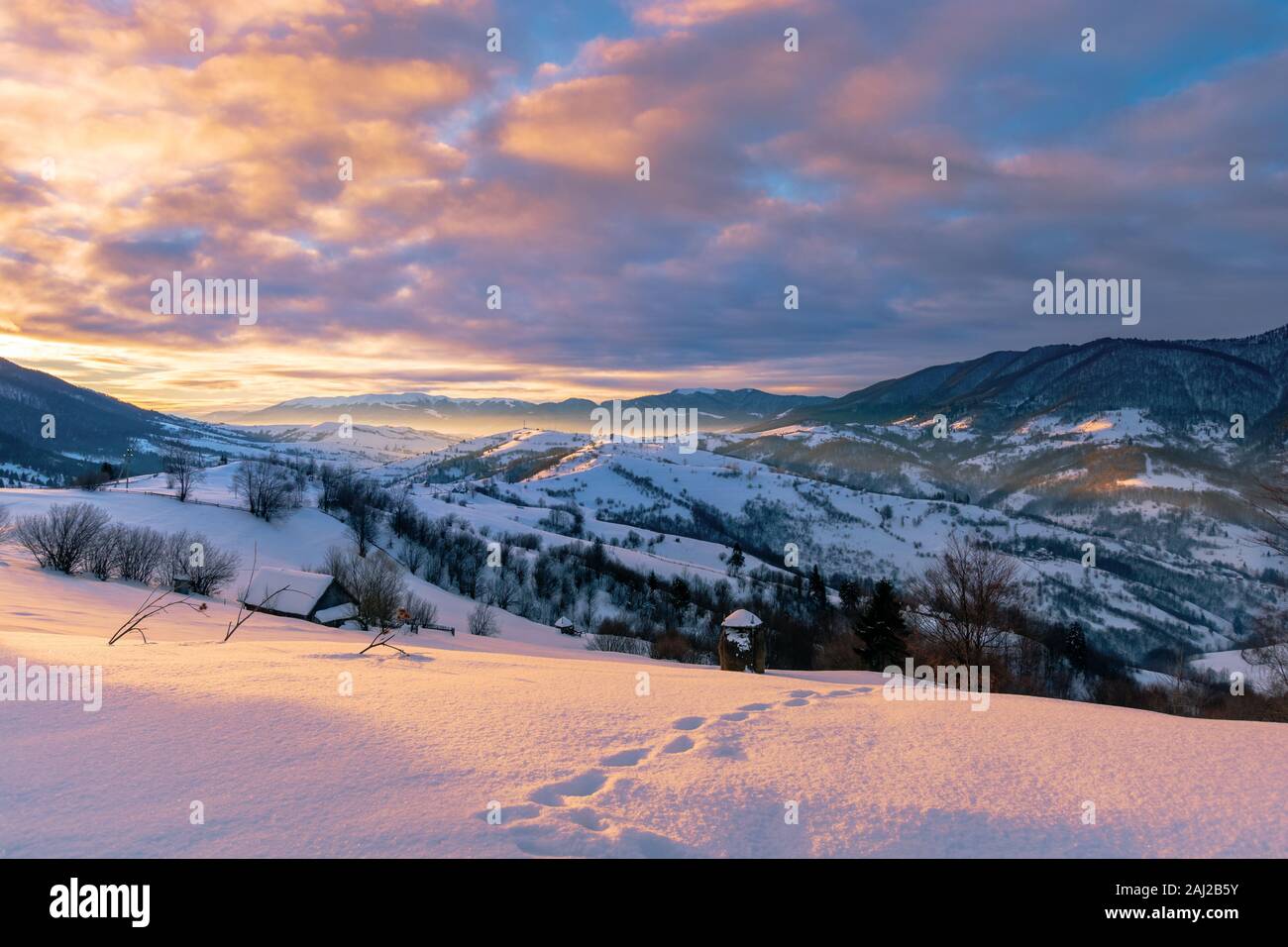 mountainous countryside in winter at sunrise. snow covered hills and fields of carpathian rural area rolling off in to the distant krasna ridge. glowi Stock Photo