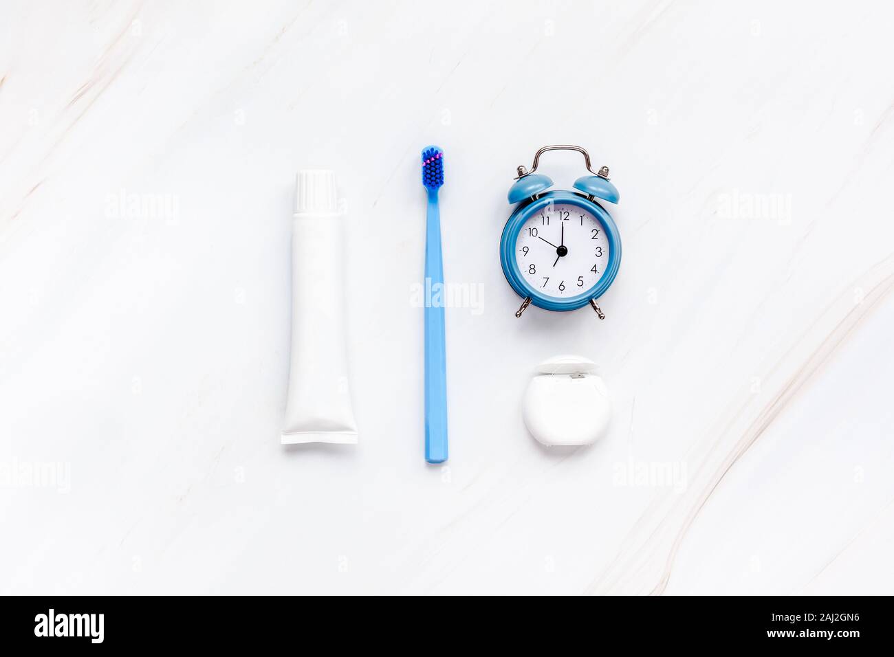 Teeth hygiene and oral dental care products with blue alarm clock on white marble table background with copy space. Blank tube of toothpaste and brush Stock Photo