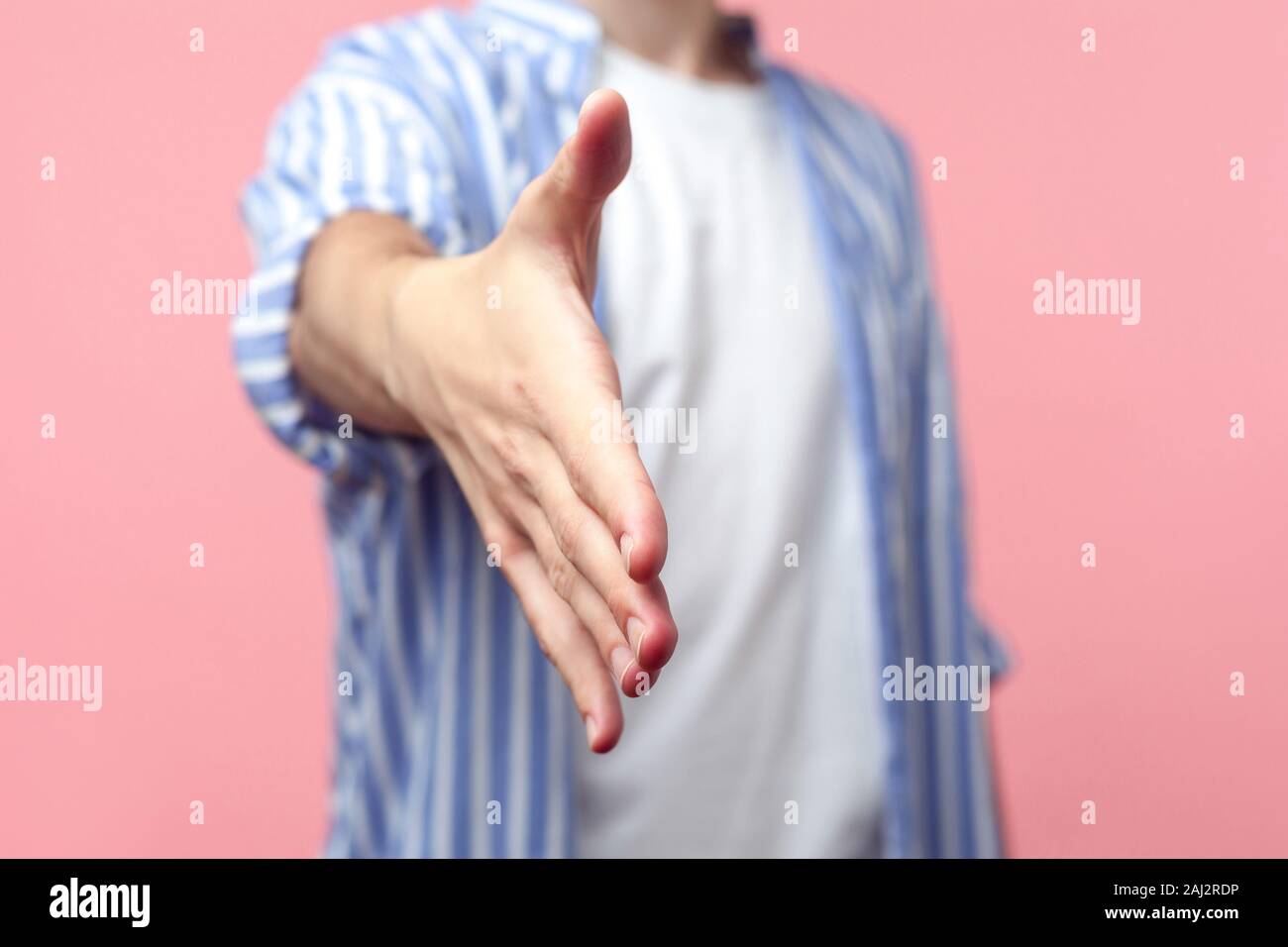 Closeup of male hand outstretched for greeting, man in casual striped shirt giving arm to handshake, welcoming at job interview, business deal. indoor Stock Photo