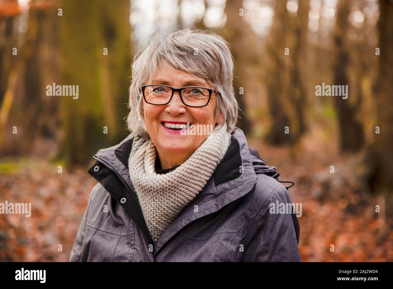 Portrait of happy, beautiful senior woman in autumn forest, looking and smiling Stock Photo