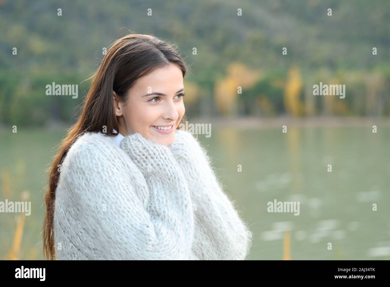 Candid girl warmly clothed with a sweater standing besida a lake looking away Stock Photo