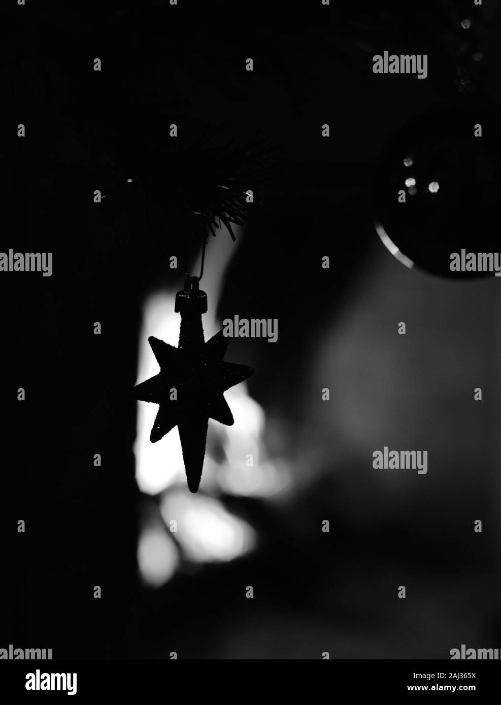 Decorative star hanging from a christmas tree against the illumination of a fireplace. Concept: Festive season. Stock Photo