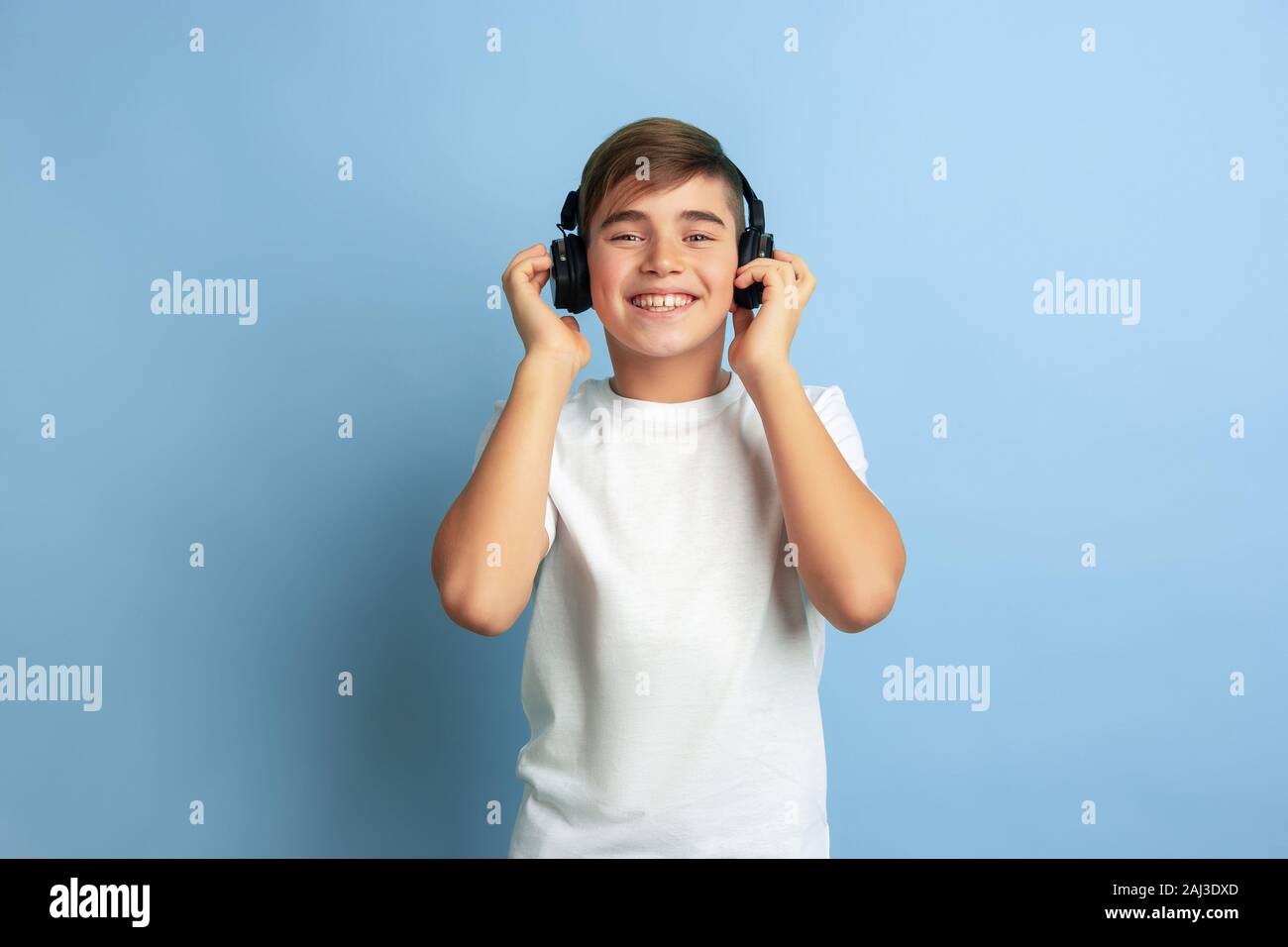 Listen to music, looks joyful. Caucasian boy portrait isolated on blue ...