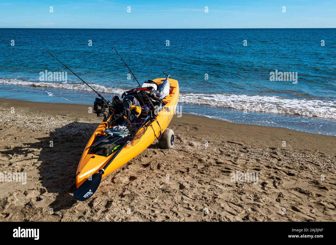 Orange sea kayak containing fishing equipment and a caught tuna fish on Cala de Mijas beach, Costa del Sol, Andalucia, Spain. Stock Photo