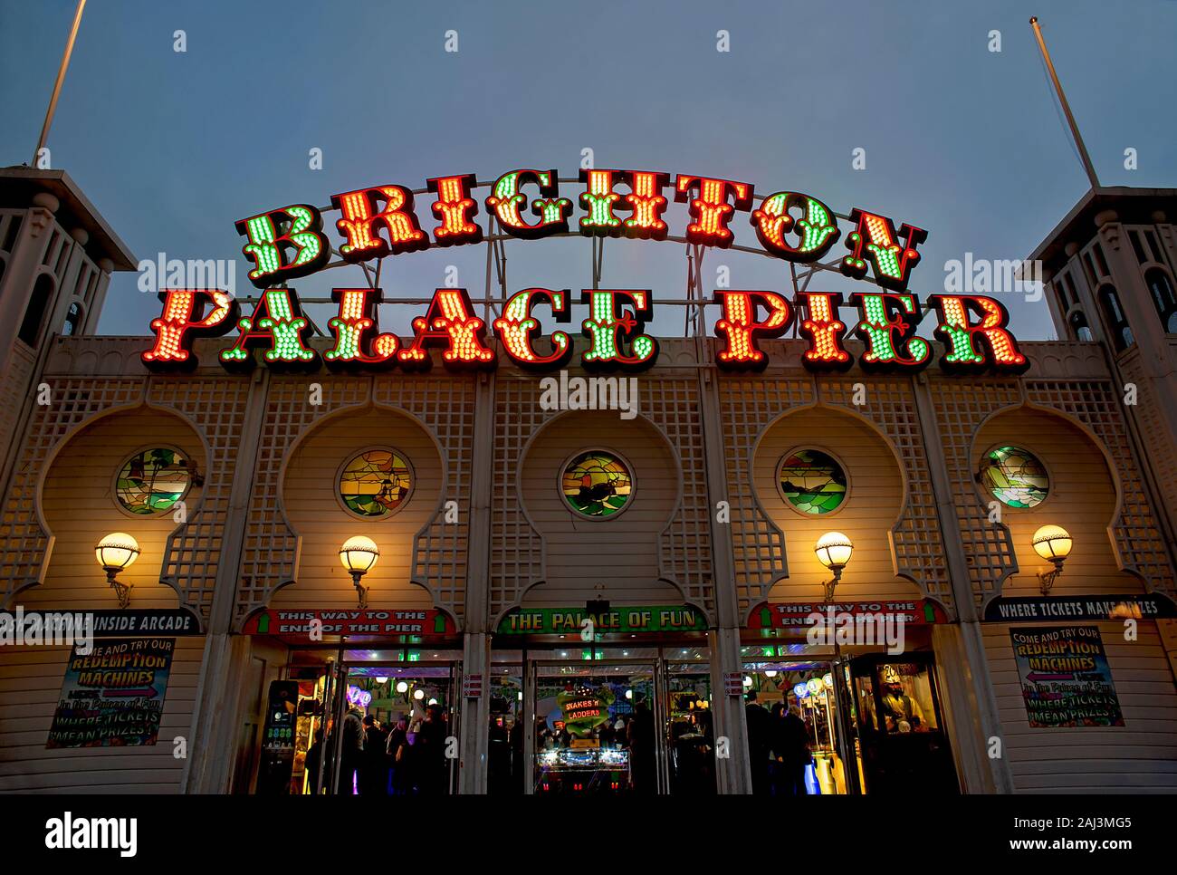 The colourful illuminated sign of Brighton Palace Pier is lit up at dusk. The famous pier in Brighton is one of the U.K.'s most popular destinations. Stock Photo